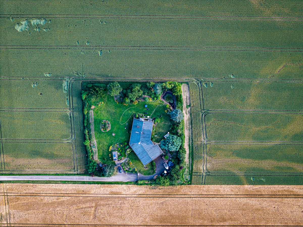 A drone hovering low over a residential property on a clear day, capturing aerial footage of the land and buildings below