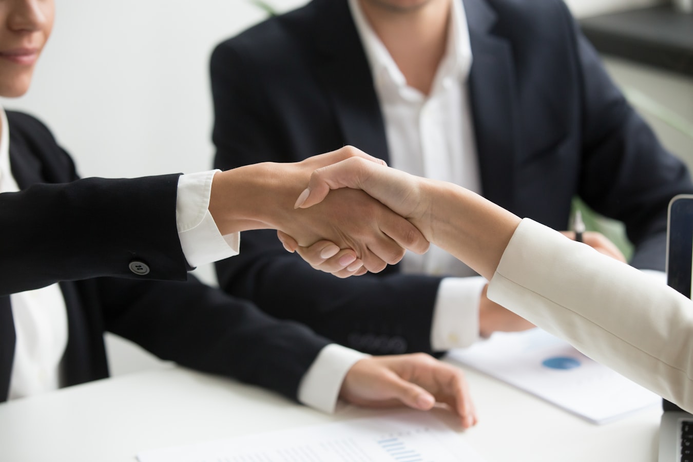 A recruiter shaking hands with a candidate across a desk in a bright modern office
