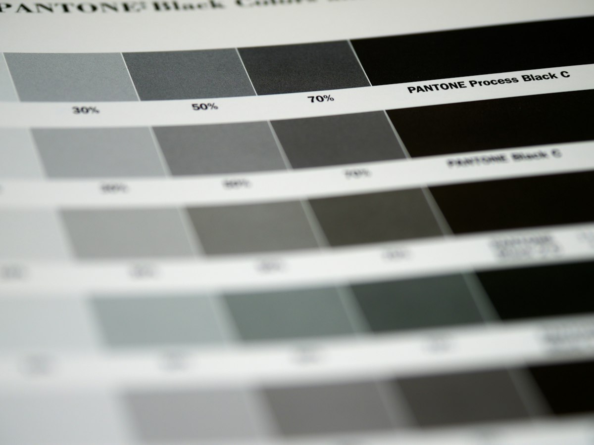 A calibrated monitor displaying a color proof next to printed CMYK swatch sheets on a prepress workstation