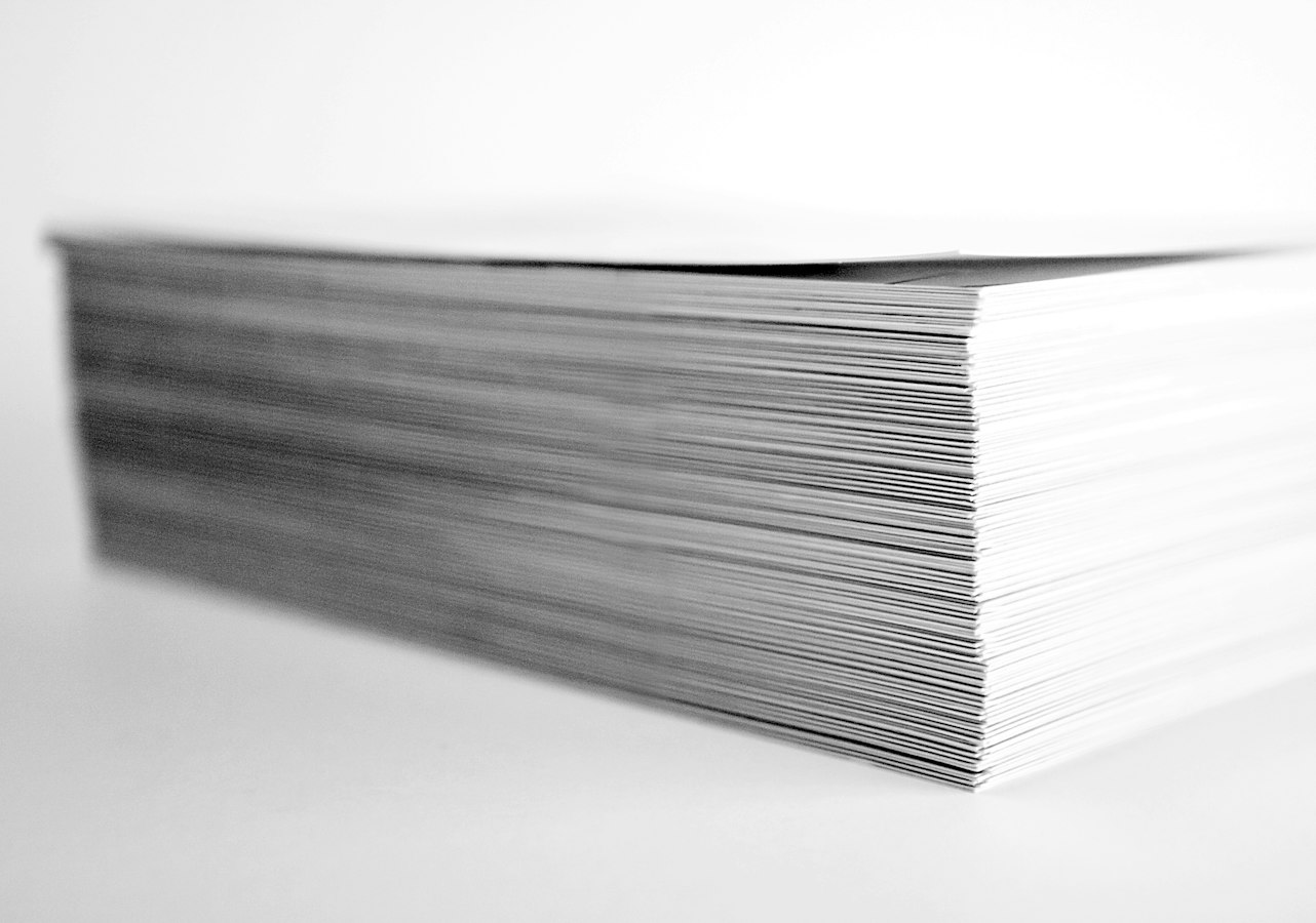 A stack of printed letterhead sheets beside an open laptop on a clean office desk